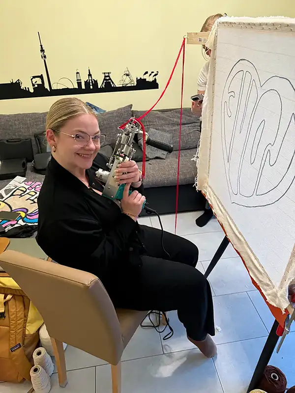 Lachende Teilnehmerin arbeitet an einem roten Herz-Teppich mit Tufting Pistole.